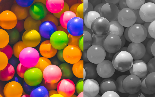 A split image of colorful plastic balls, with the left side showing vibrant colors like pink, orange, green, and blue, and the right side in grayscale, illustrating a comparison between color and monochrome vision