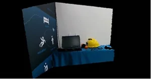 LIPSedge™ AE430 Industrial 3D Camera with Edge Processing Capability 4 A small exhibition setup featuring a laptop, a yellow safety helmet, and an orange ball on a blue table, positioned against a white and blue backdrop with industrial-themed icons and graphics.