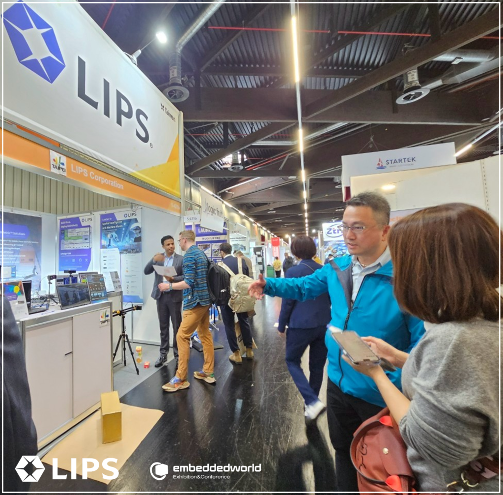 LIPS Corporation booth at Embedded World Exhibition showcasing advanced technology solutions with professional staff in blue uniforms demonstrating products to international visitors in modern industrial exhibition hall